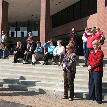 People sitting on the steps of the COMS building listening to Taps